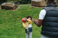 Content African American kid playing with red ball with unrecognizable black father while spending time in grassy park during weekend