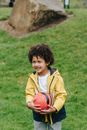 Delighted African America kid with Afro hair looking away while standing on green meadow with football in hands