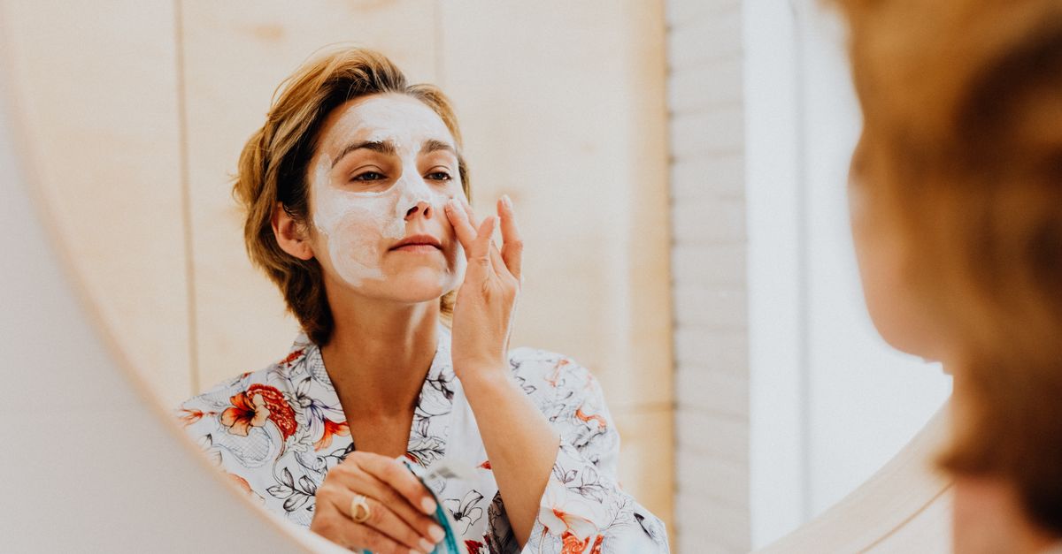 A woman applying a cosmetic mask for skincare in front of a mirror.