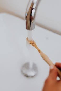 Close-up of a bamboo toothbrush being rinsed under a faucet, emphasizing sustainable dental care.