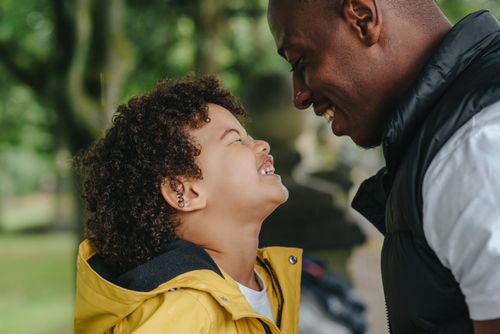 Free Side view of African American young father smiling while looking on joyful little son with closed eyes on blurred background Stock Photo
