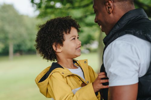 Free Side view of crop smiling African American father talking to charming child on street while looking at each other Stock Photo