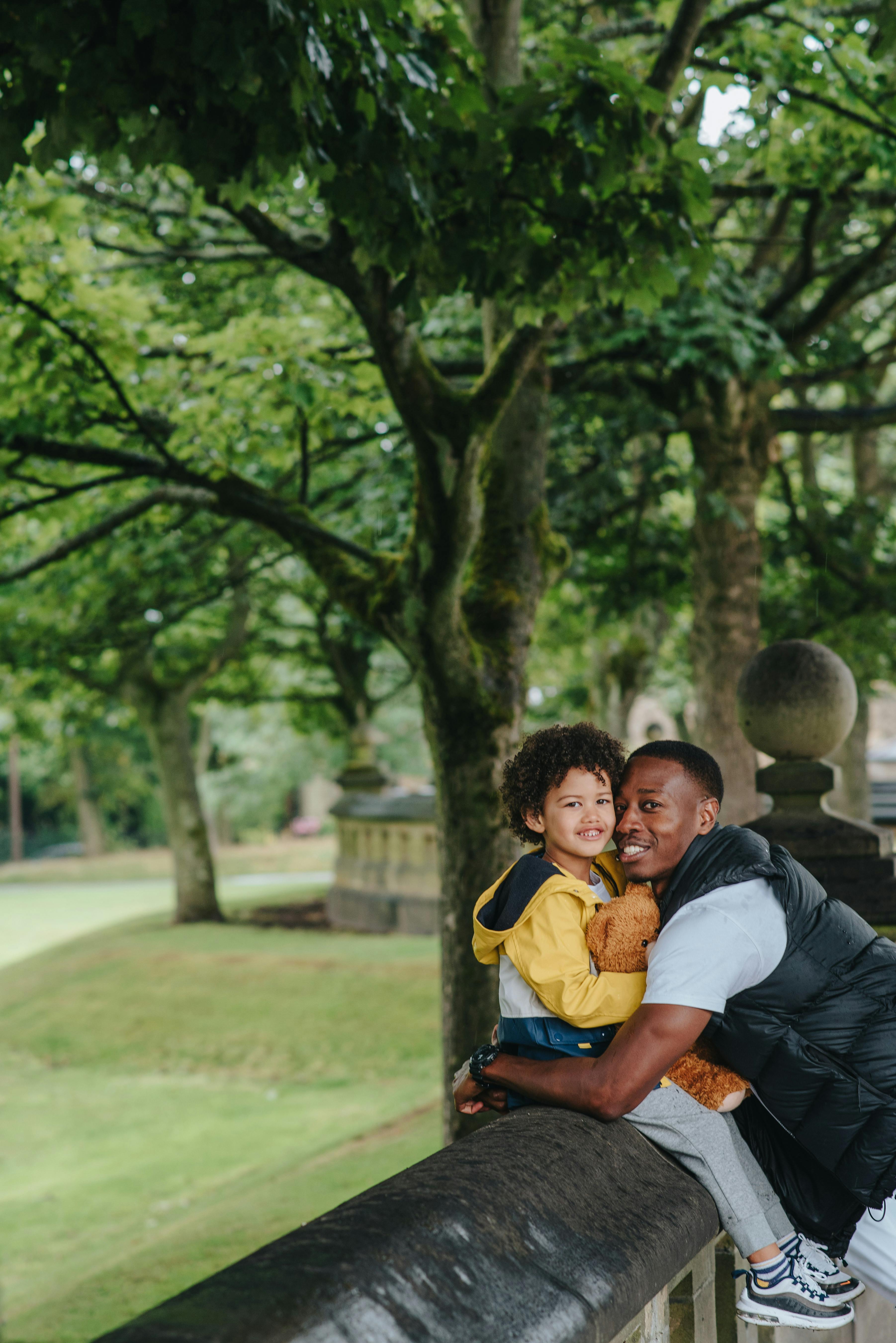 Side view of content African American man embracing son in casual wear while looking at camera in town