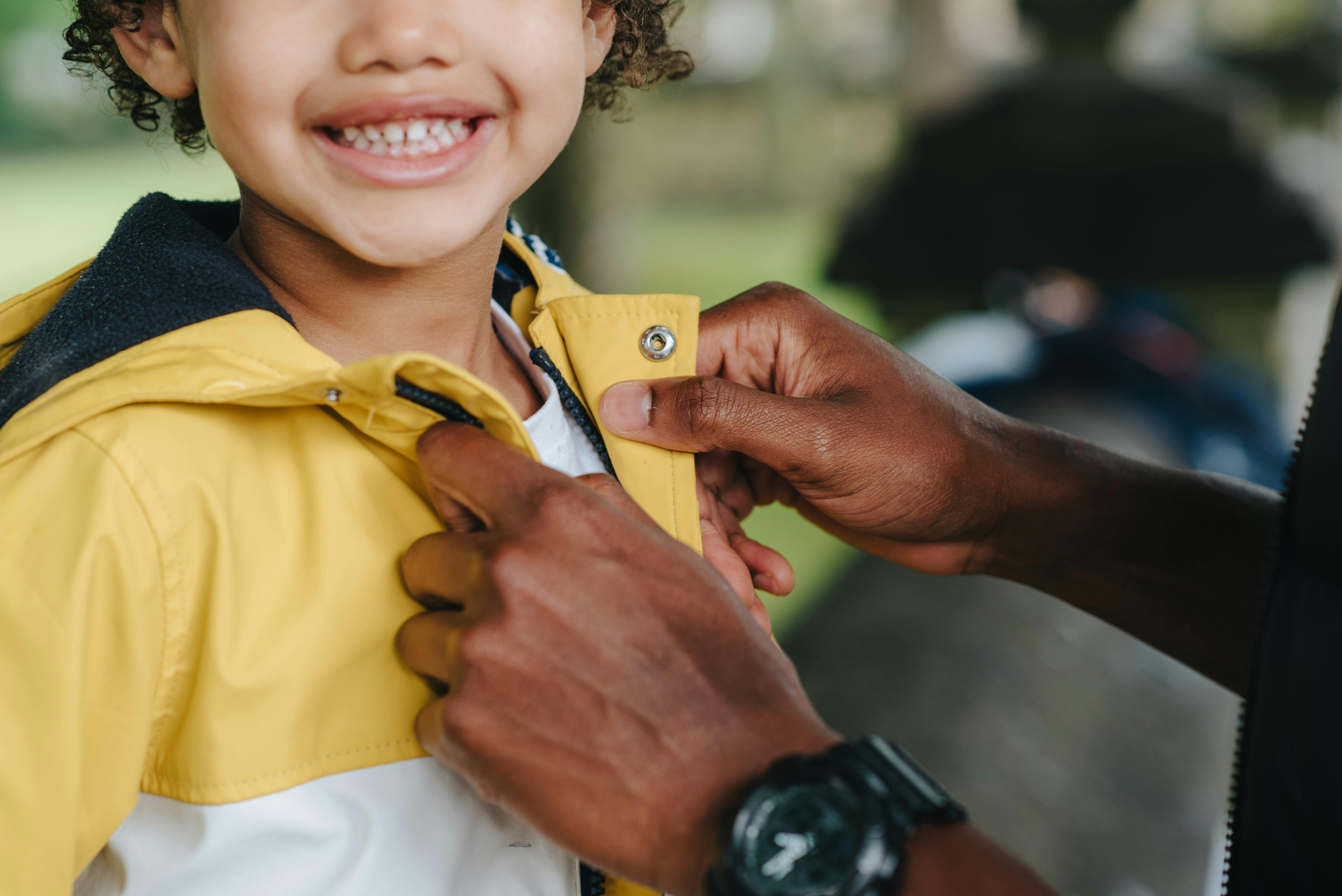 crop black father buttoning up jacket of candid son outdoors