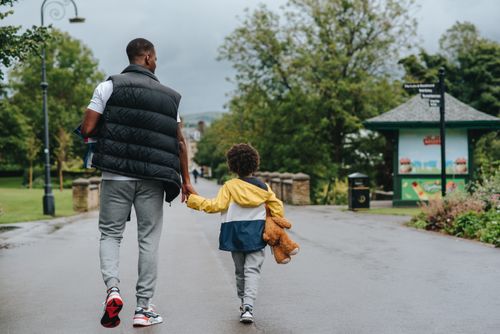Free Back view of anonymous African American man holding child by hand while walking on urban roadway in daylight Stock Photo