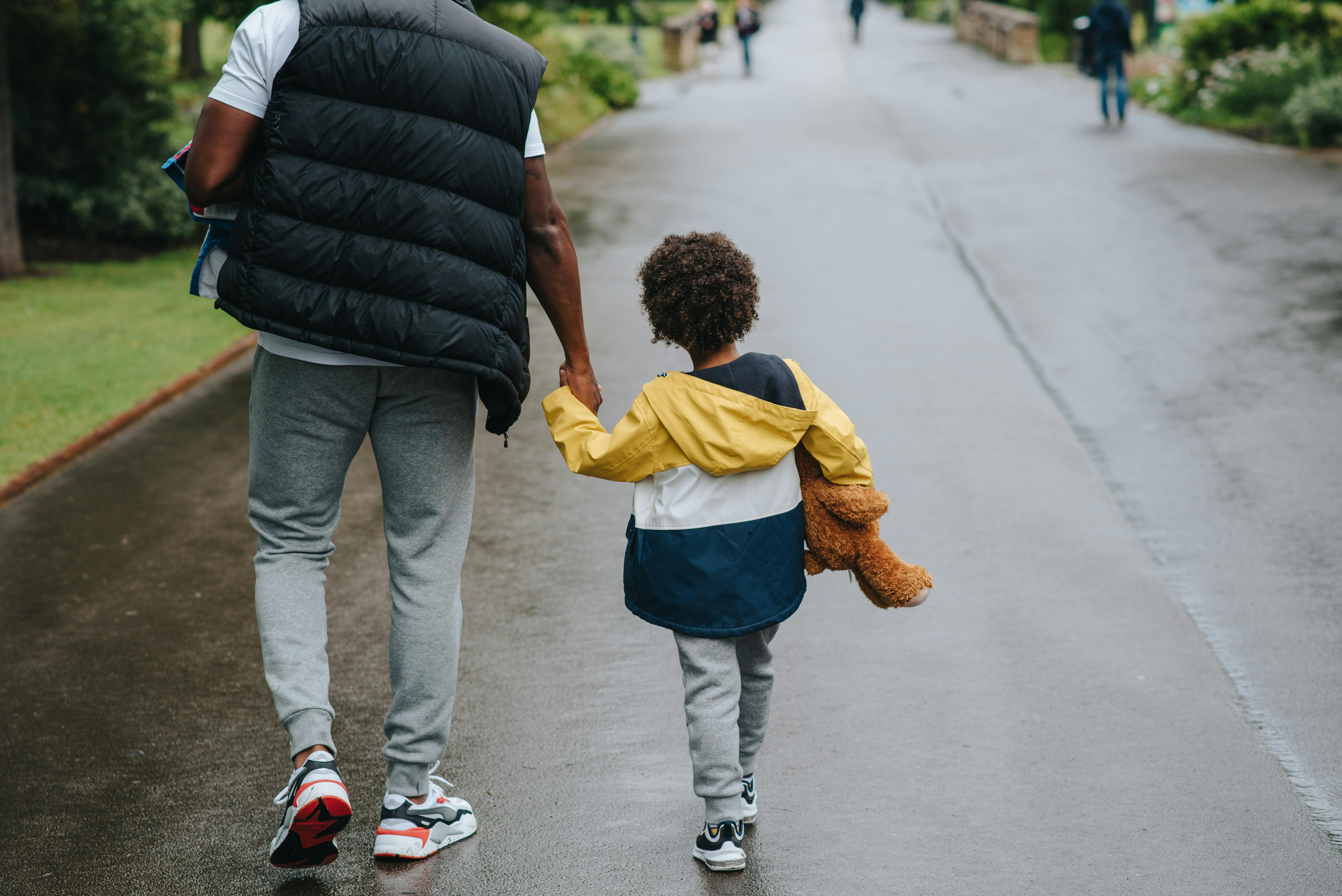 crop black man with son holding hands strolling on roadway