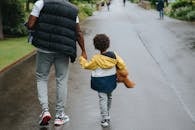 Crop black man with son holding hands strolling on roadway