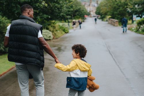 Free Back view of anonymous African American man holding cheerful son by hand while looking at each other on urban road Stock Photo