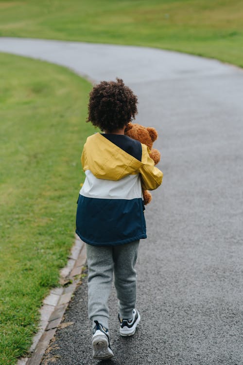 Unrecognizable ethnic boy with toy bear strolling on walkway