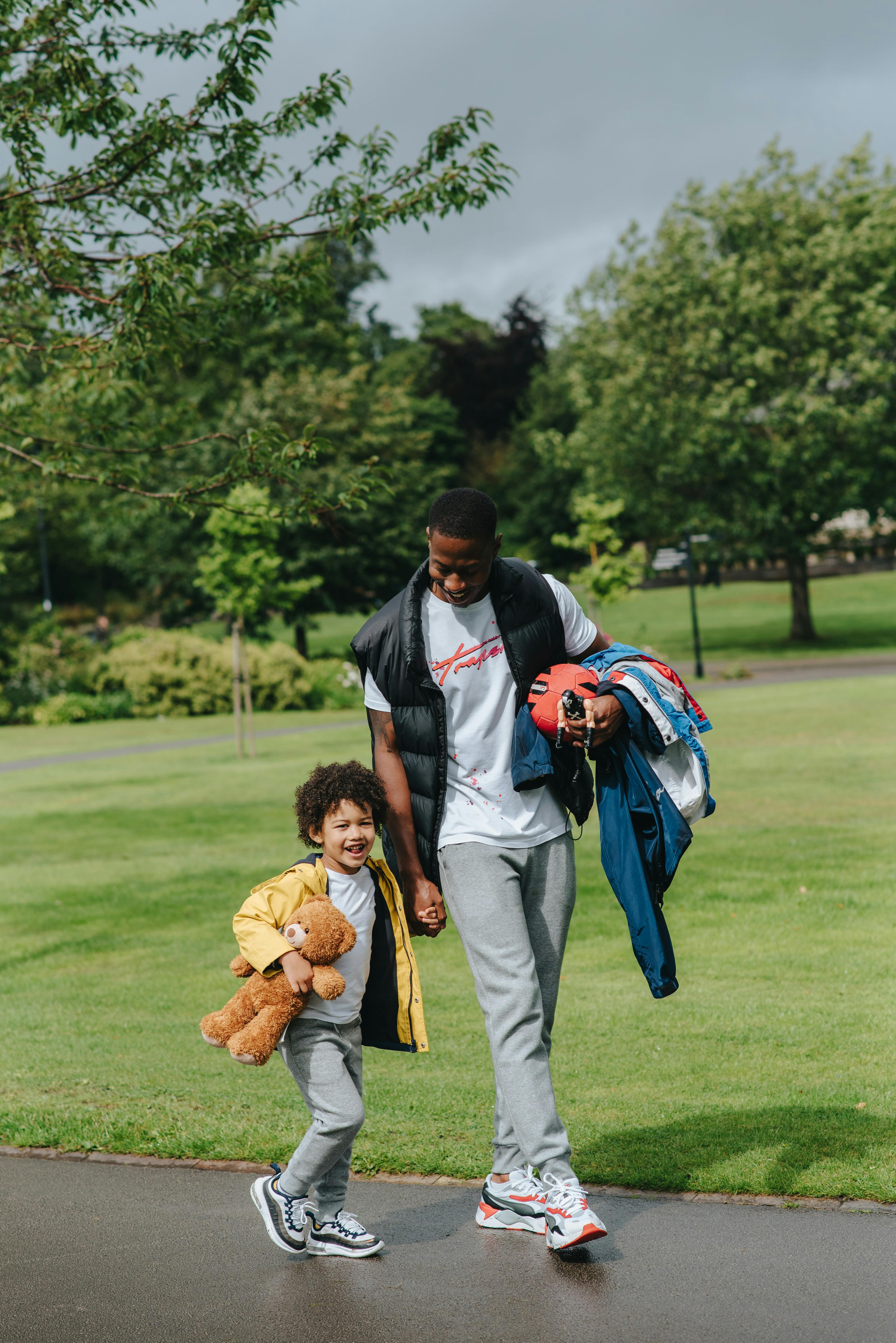 black man with happy boy walking on road near park