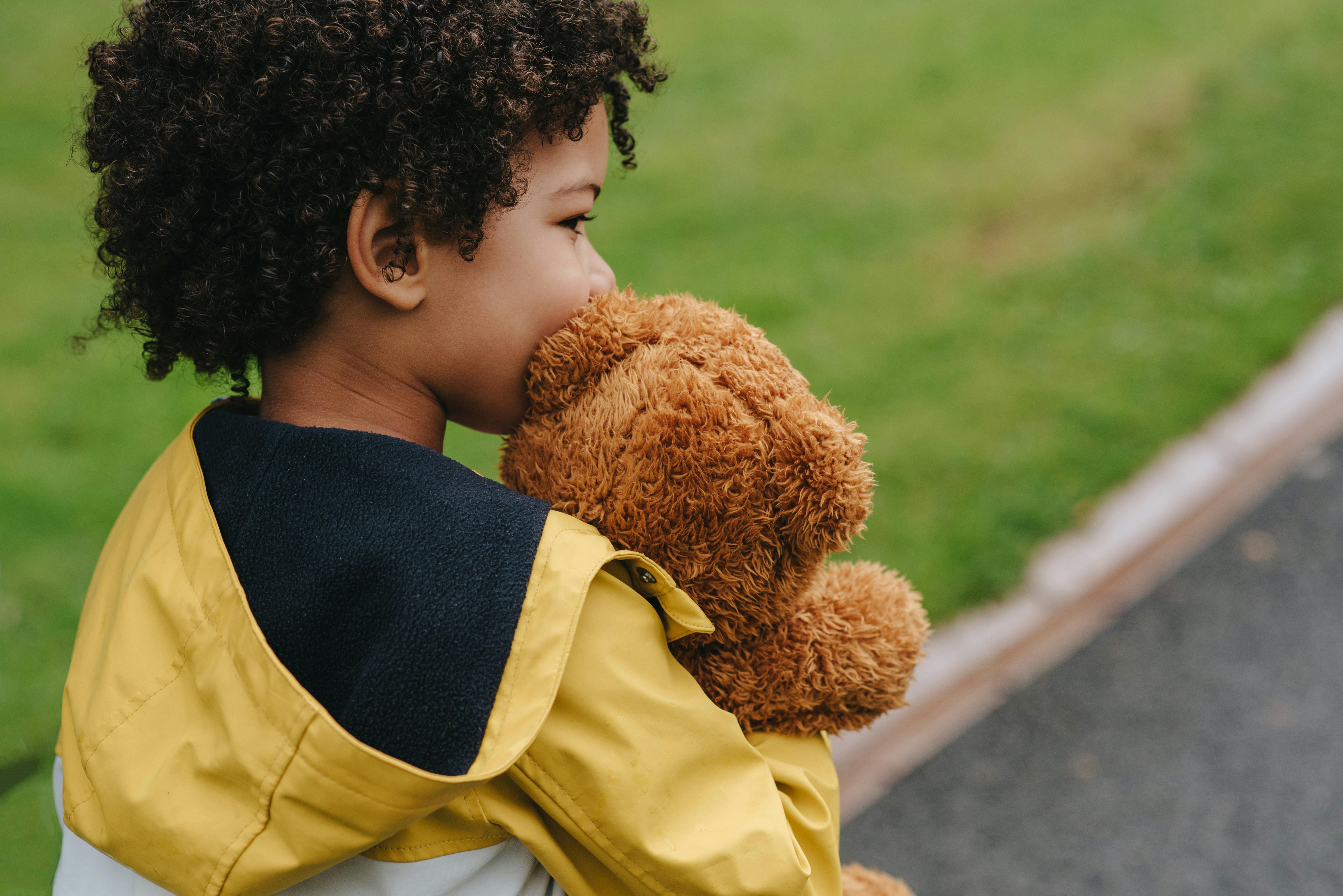 crop charming ethnic boy with soft toy near urban lawn