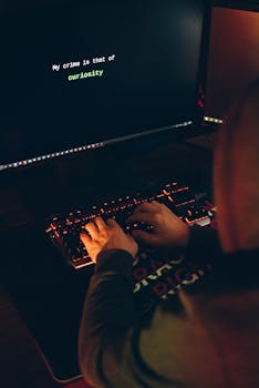 A person in a hoodie typing on a keyboard with a computer screen displaying a curiosity message.