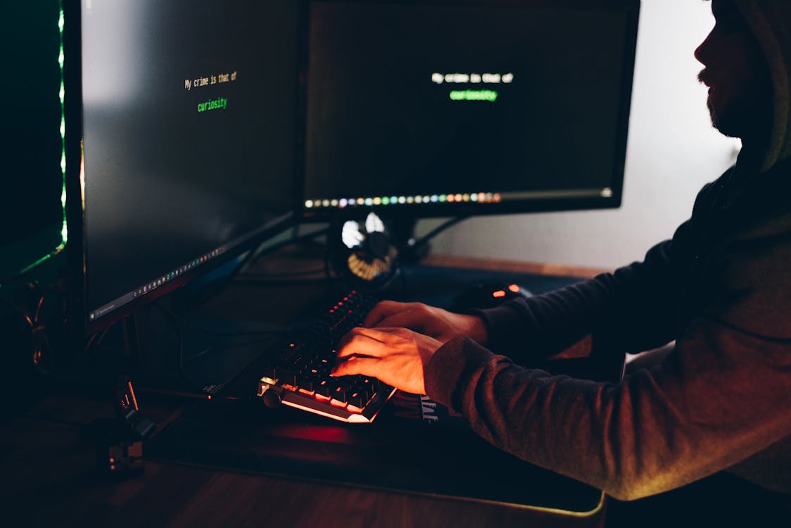 Crop hacker silhouette typing on computer keyboard while hacking system