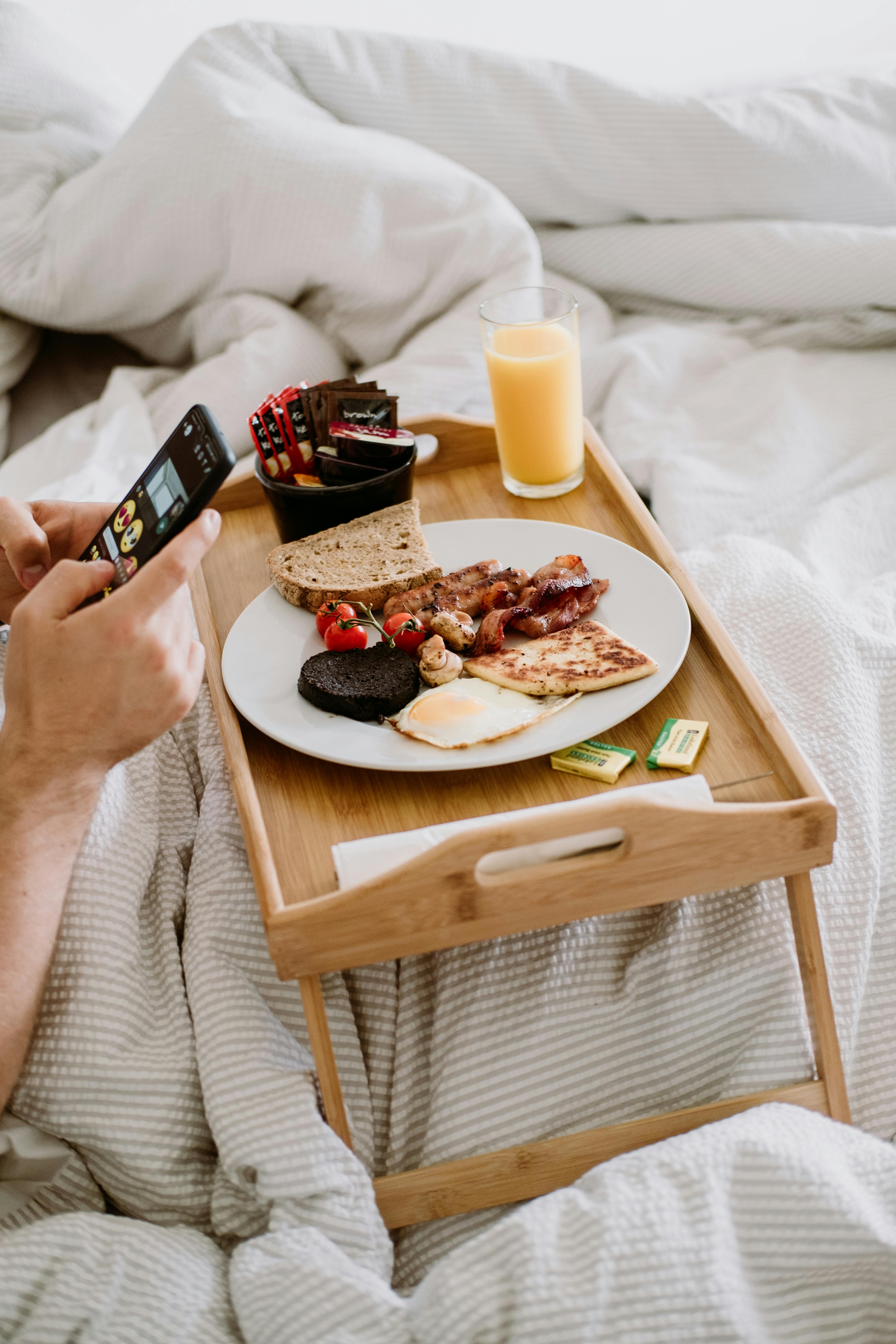 crop person with smartphone and delicious breakfast in bed
