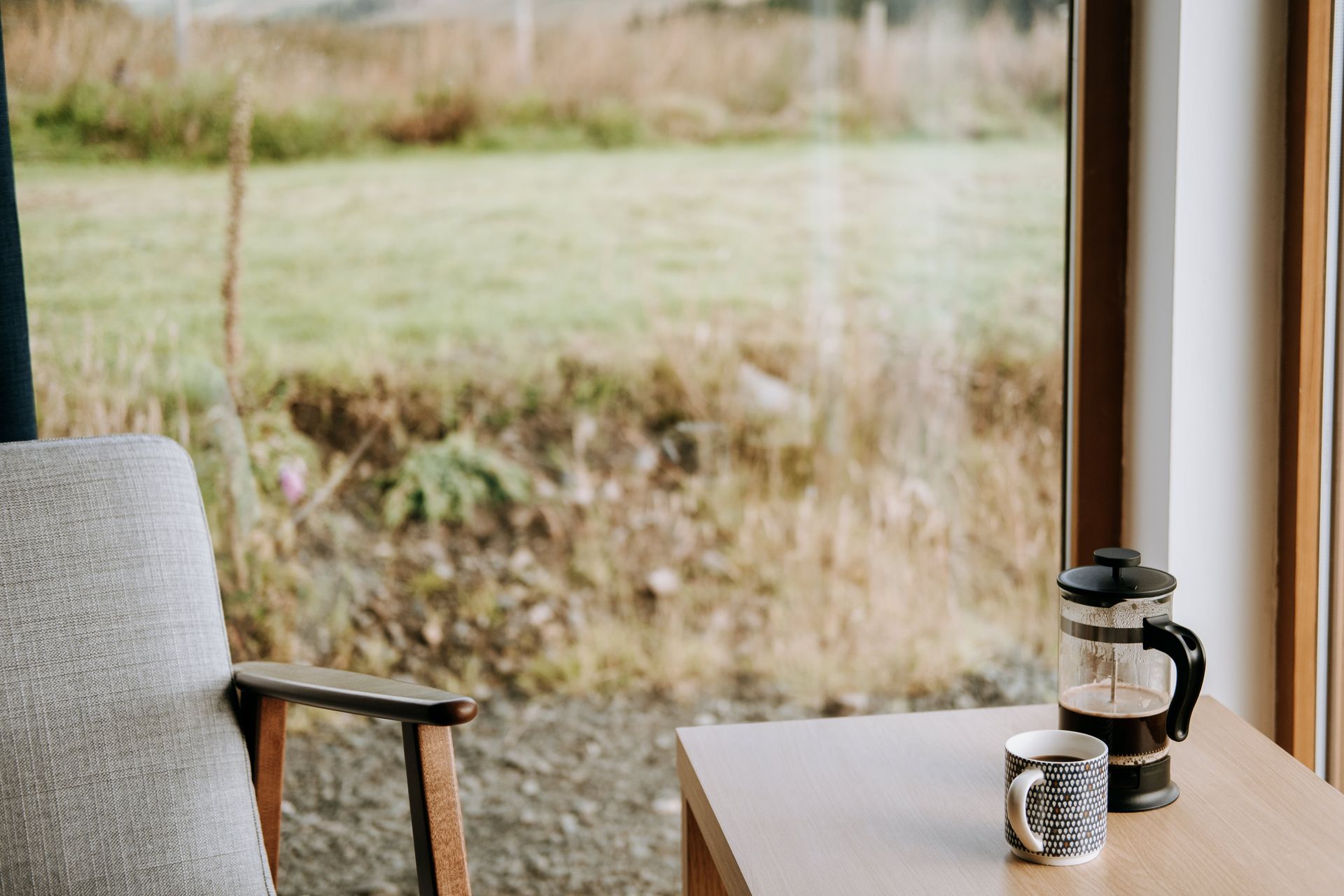 French press with aromatic espresso near ornamental mug on table against glass wall in countryside house
