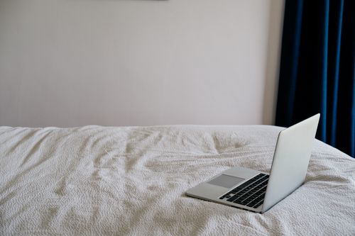 Free Open netbook on creased bed cover near wall with curtain in house in daytime Stock Photo
