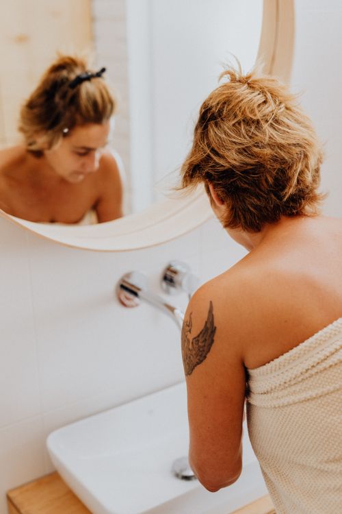 Free Woman wrapped in towel washes face at bathroom sink, reflecting self-care habits. Stock Photo