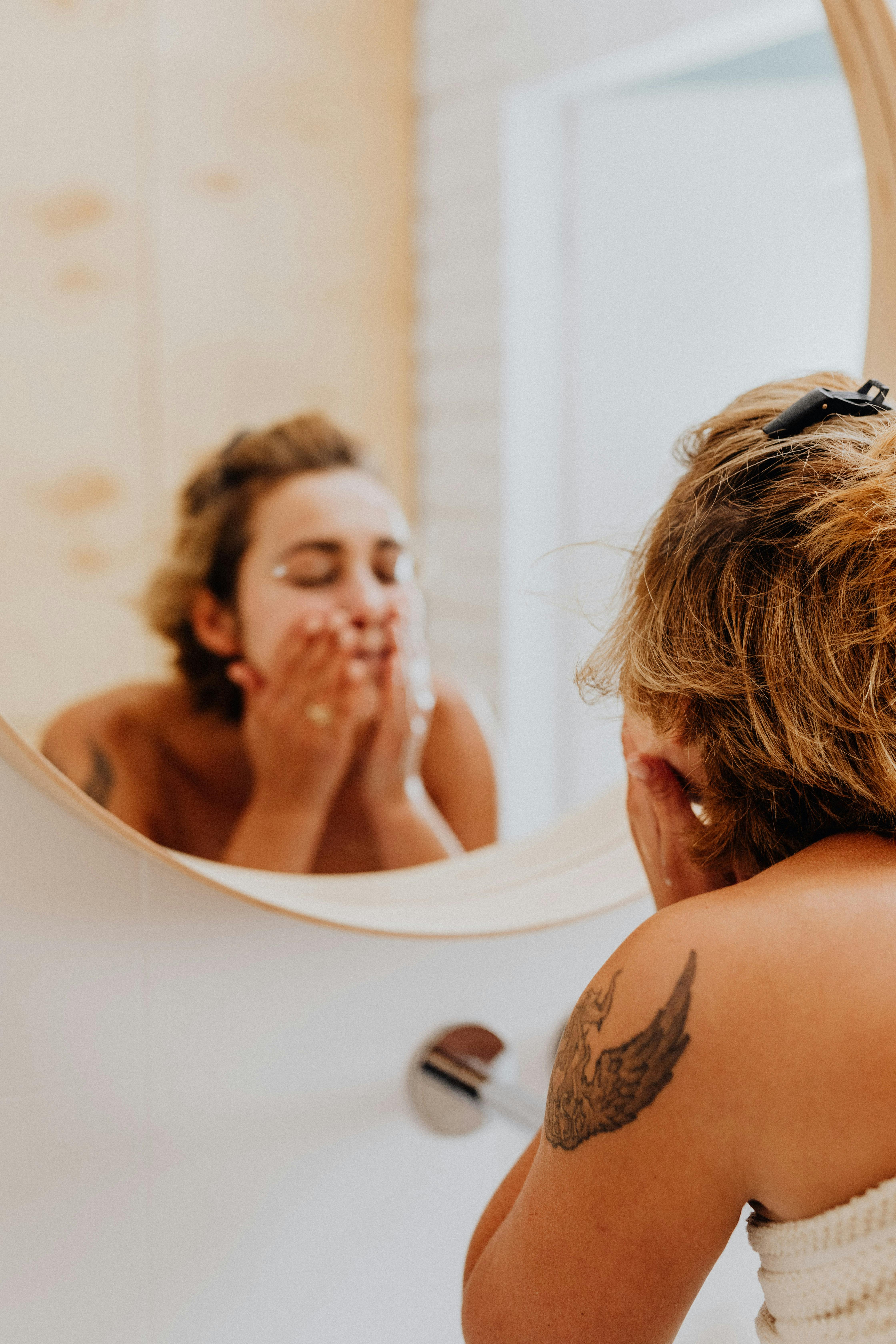 Woman washing her face with skincare products while looking in the bathroom mirror.