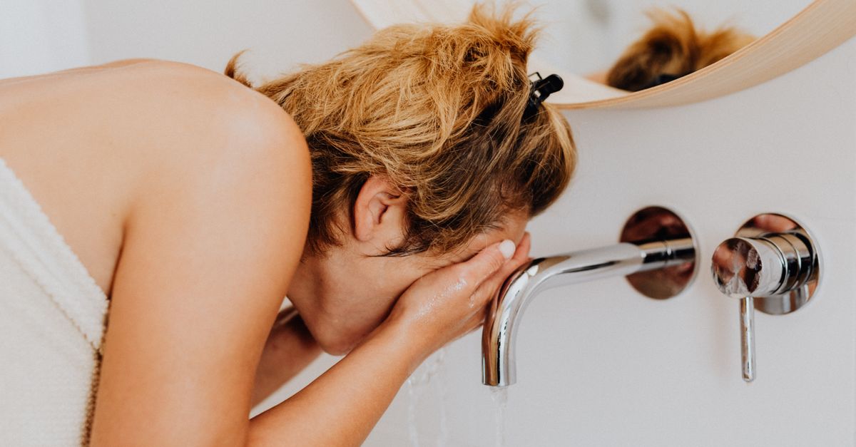 person splashing cold water on their face in a bathroom mirror