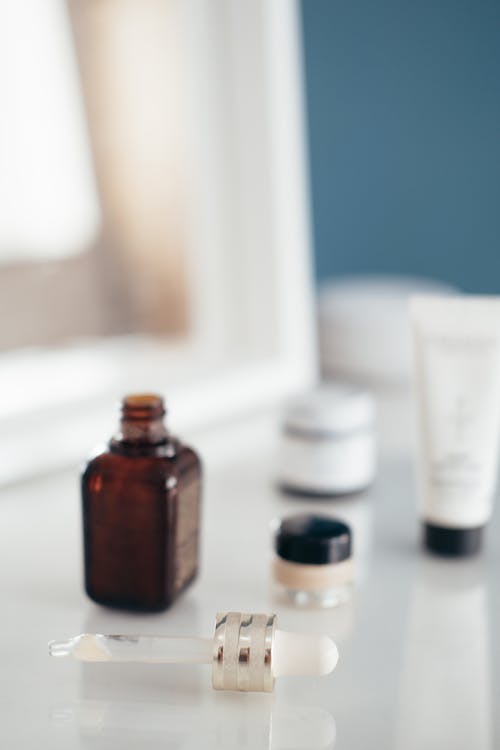 Small open bottle of aroma oil near different beauty products on white table in daytime