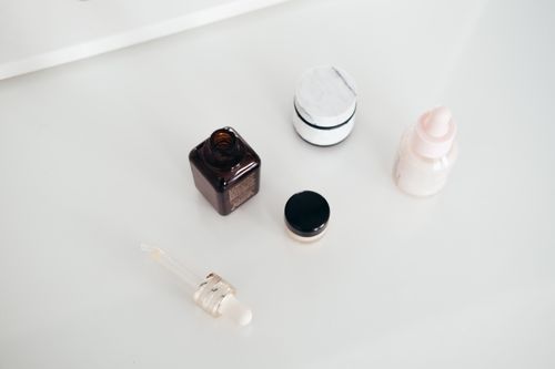 Skincare jars, a dropper and a small bottle on a smooth white surface