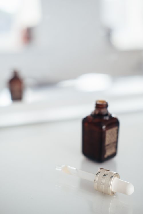 A dark glass serum bottle next to a pipette on a reflective surface