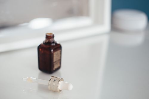 An open serum flacon beside a glass dropper on a bright table