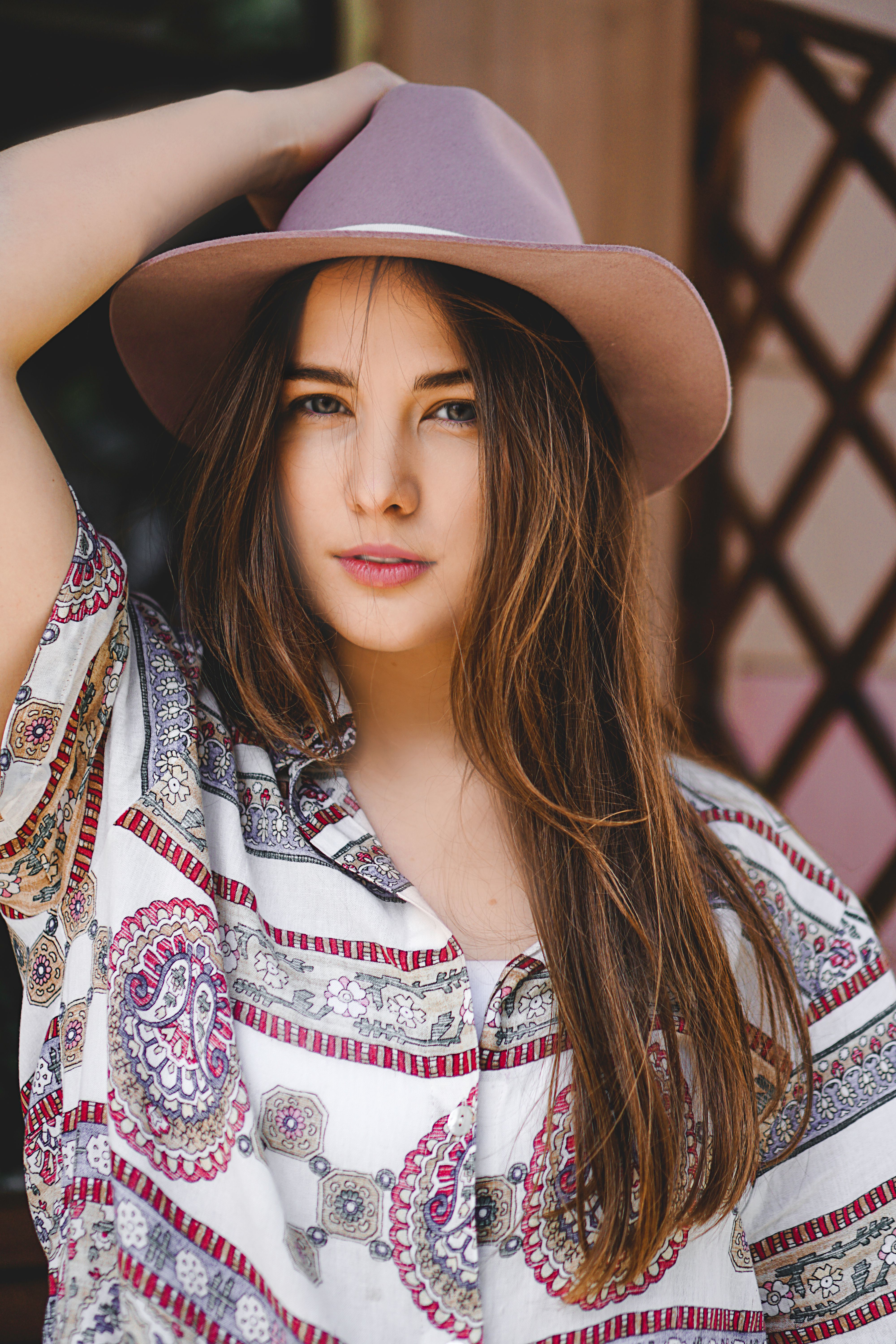 Portrait of a fashionable woman wearing a patterned shirt and a hat outdoors.