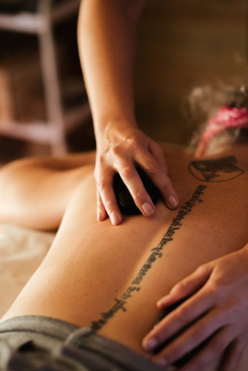 Free From above of crop masseuse with anonymous woman using stone during massage therapy in spa salon Stock Photo