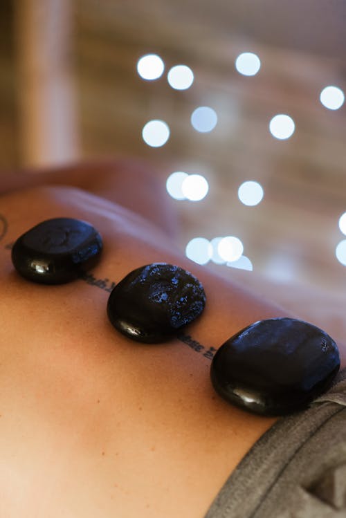 Free From above of crop anonymous tattooed client with basalt massage rocks on back in spa salon with glowing lights Stock Photo