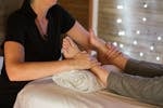 Unrecognizable masseuse therapist giving feet massage to anonymous female client lying on table with legs on towel in spa on blurred background