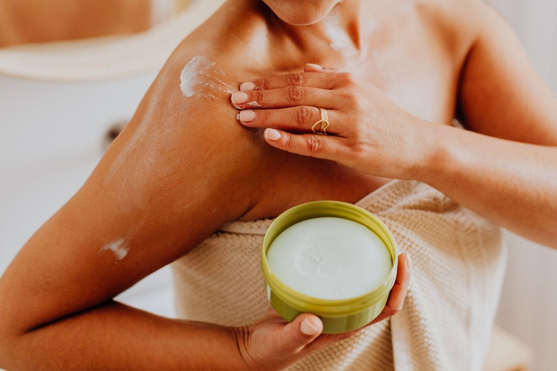 Woman applying body cream to shoulder for skin care and moisturizing
