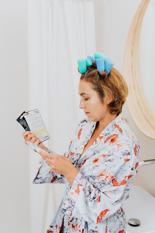 Free Woman Reading Etiquettes of Face Masks While Wearing a Bath Robe and Hair Curlers Stock Photo