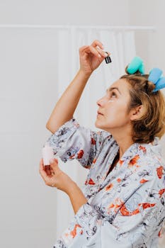 Woman applying skincare serum with rollers in hair, showcasing morning beauty routine.
