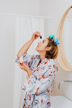 A woman in a bathroom applies serum, focusing on skincare. Bright and clean aesthetic.