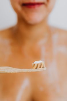 Woman holding a bamboo toothbrush with toothpaste. Focus on sustainable oral hygiene.