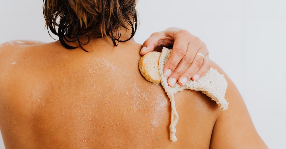 Back view of a person scrubbing their shoulder with a loofah sponge emphasizing personal care.