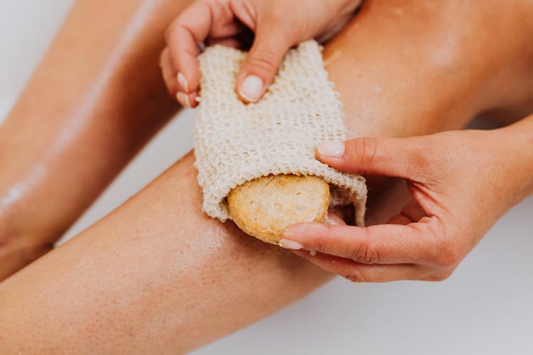 Person Using A  Loofah Body Scrub Sponge On Legs