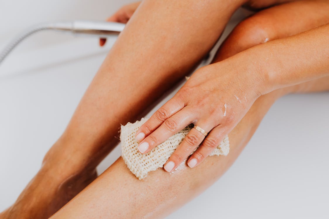 Person Using Loofah Body Scrub Sponge on Leg