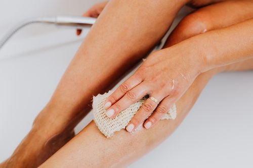 Free A close-up shot of a hand scrubbing a leg with a loofah, perfect for skincare and personal hygiene themes. Stock Photo