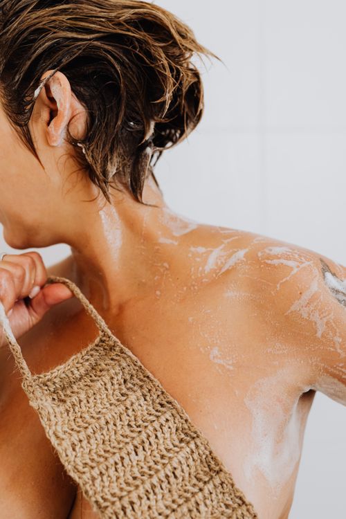 Free Woman enjoying a shower, using an exfoliating scrub for smooth skin care and relaxation. Stock Photo