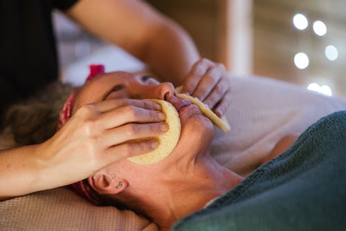Free Adult lady in towel getting face massage with sponge from massager in spa Stock Photo
