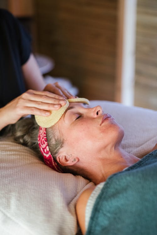 Free Adult female lying in spa center and getting face massage with sponge from massager Stock Photo