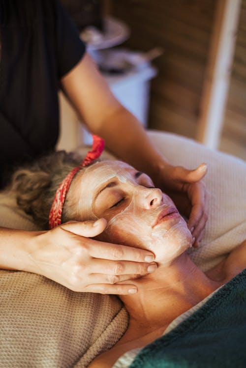 Free Adult female with mask on face getting massage while lying in spa center Stock Photo