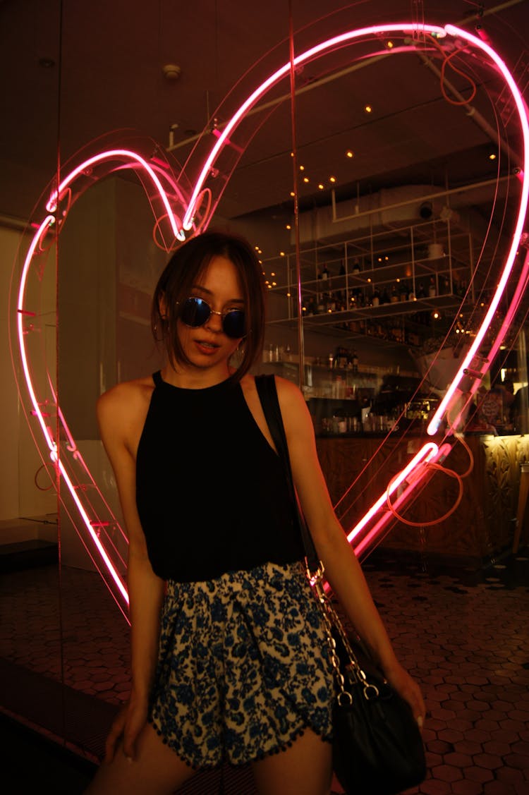 A Woman Standing Near Neon Signage While Posing At The Camera