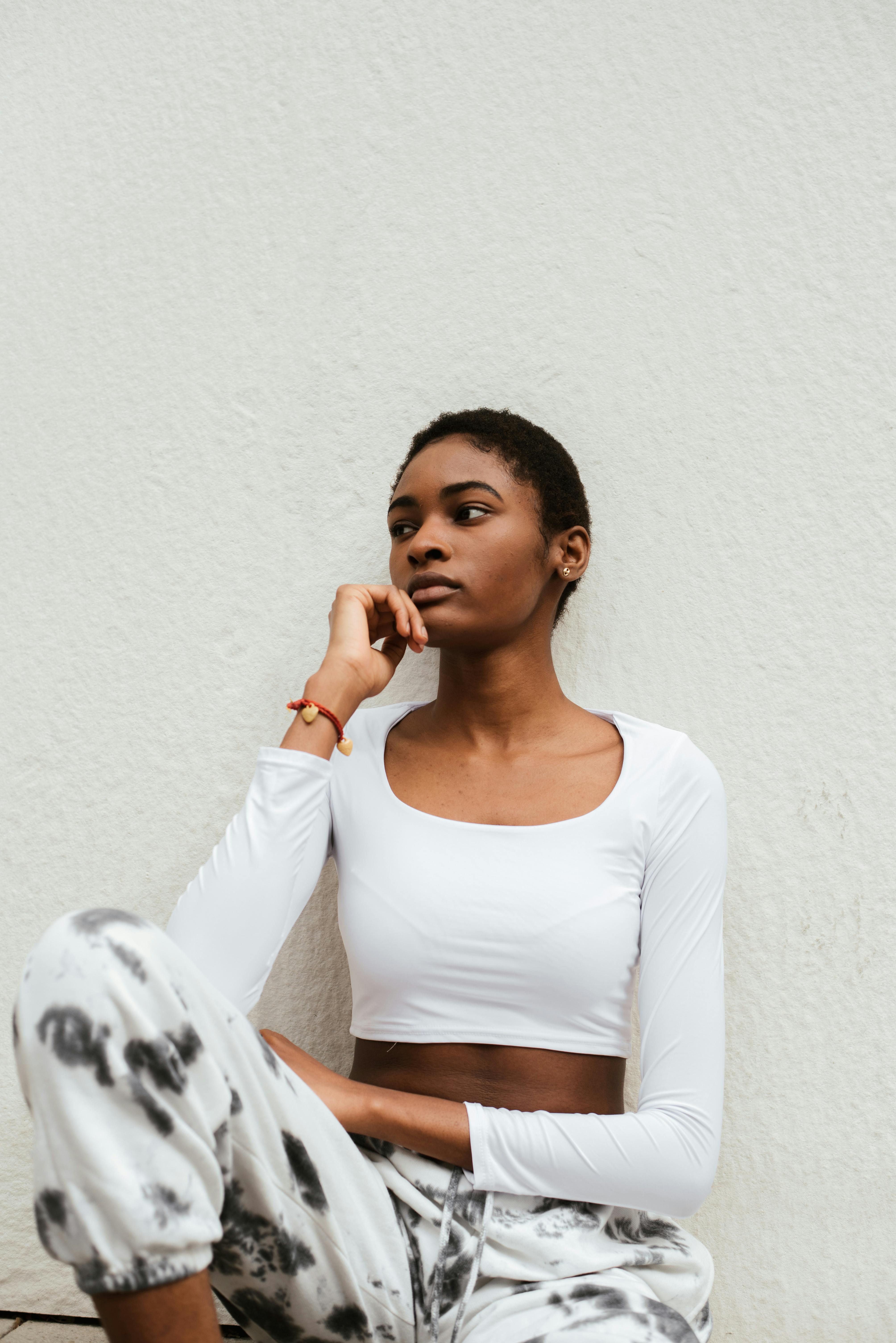 一位穿着时髦服装、留着短发的非裔美国女性神情严肃地坐着，手托下巴，面容难以看清