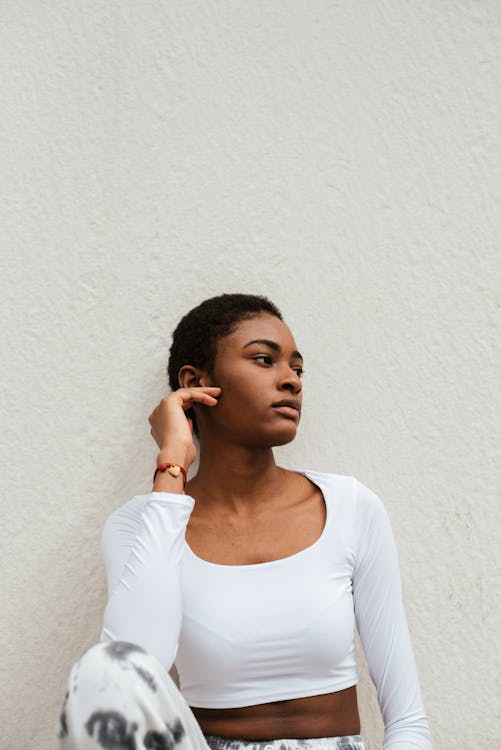 African American female in casual clothes relaxing near wall while touching face and looking away
