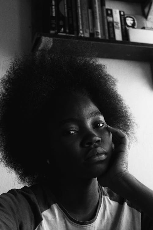Contemplative black woman leaned on hand near bookshelf