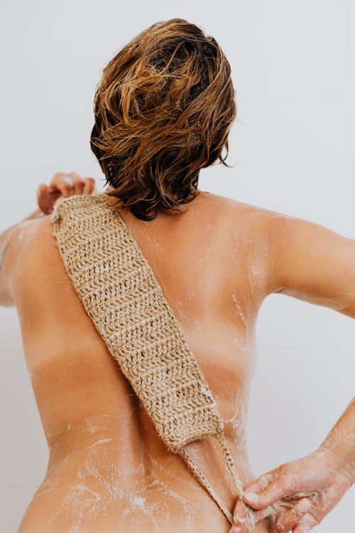 Free Woman exfoliating her back using a natural loofah in a clean, minimalist bathroom setting. Stock Photo