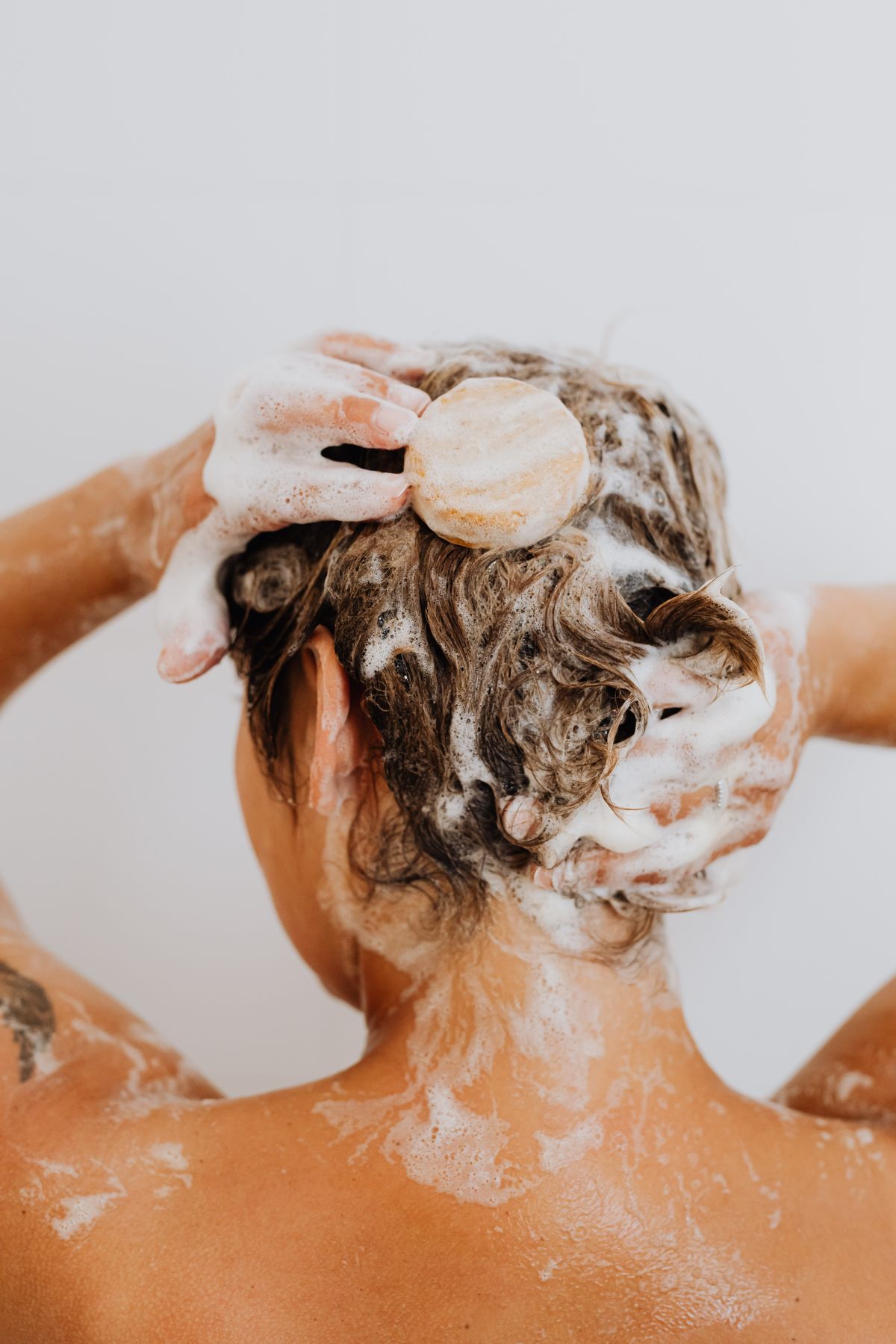 Mulher lavando o cabelo com shampoo durante o banho